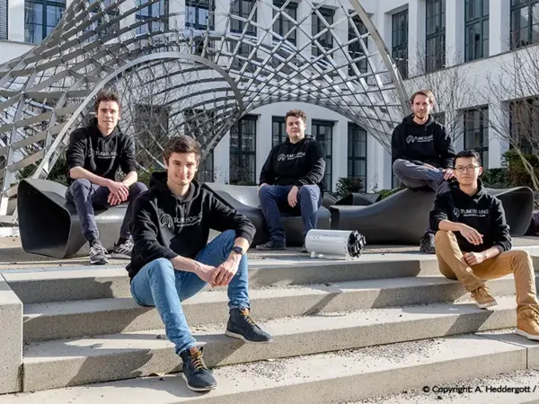 Fünf TUM Boring Mitglieder in Hoodies sitzen auf Treppen vor der technischen Universität München.
